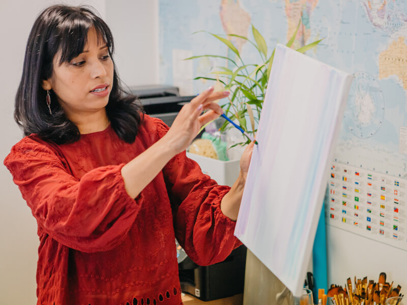 A teacher holds up a canvas to show their class how to paint.
